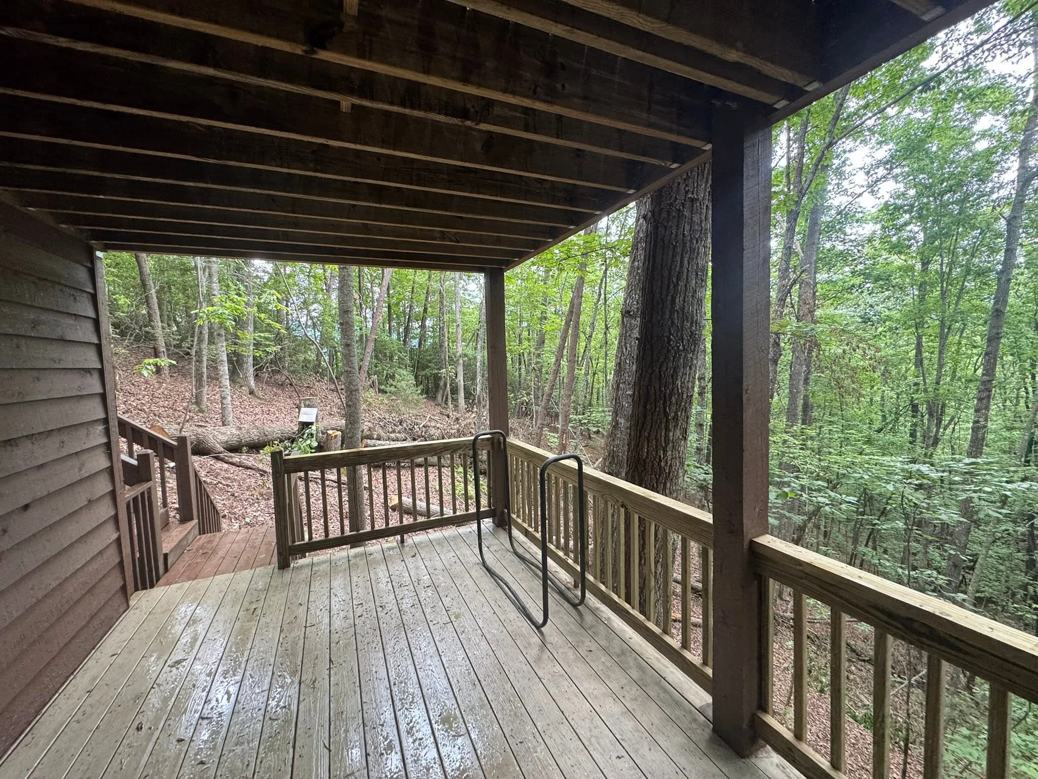 Covered wooden deck with railings overlooking wooded forest hillside
