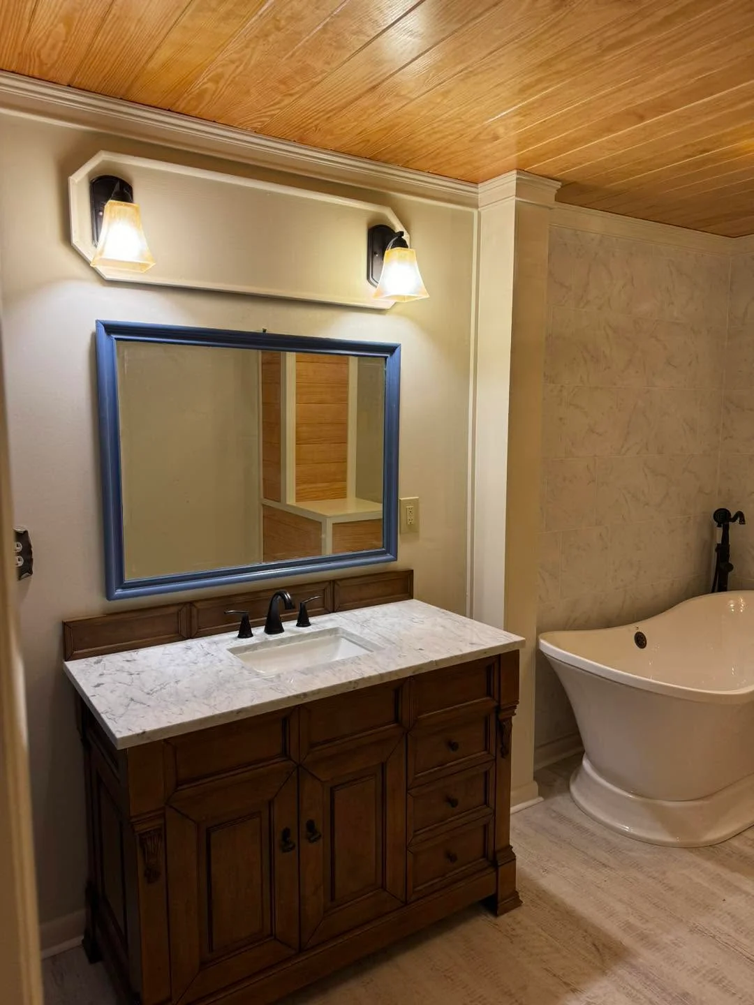 Master bathroom with dark wood vanity, marble countertop, blue mirror frame, and freestanding tub