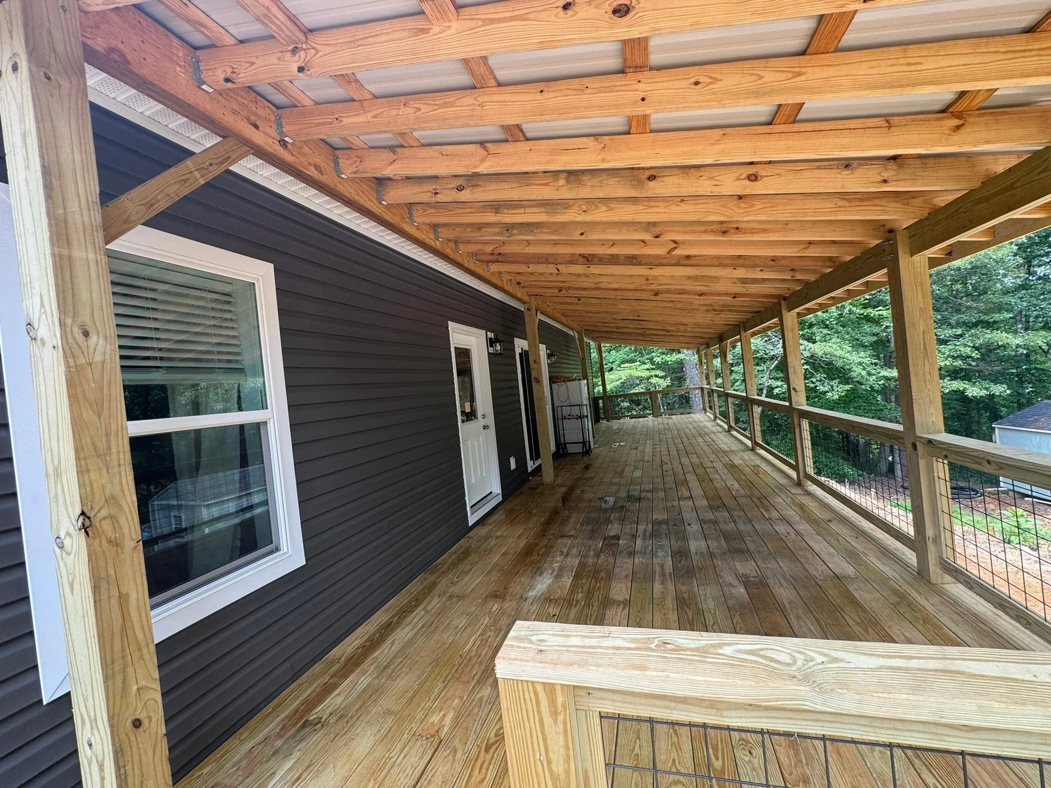 Covered deck with wooden beams, composite decking, and cable railings overlooking wooded area