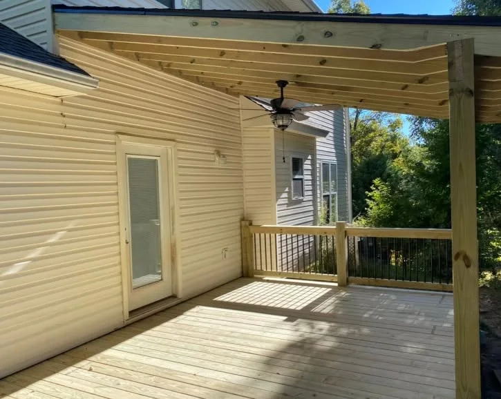Pressure-treated wood deck with pergola overhead and black metal railing system