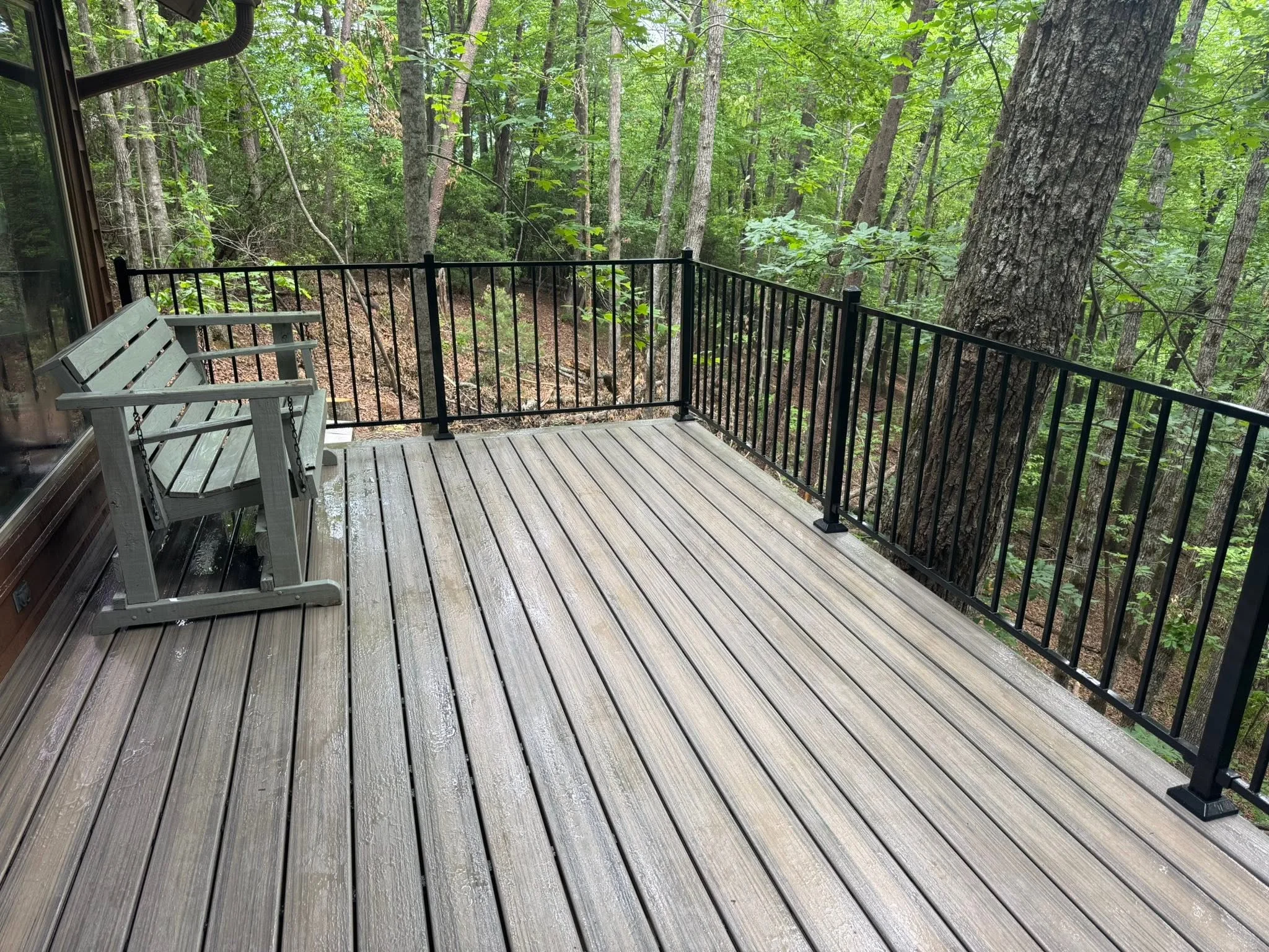 Gray composite deck with black metal railing overlooking forest canopy