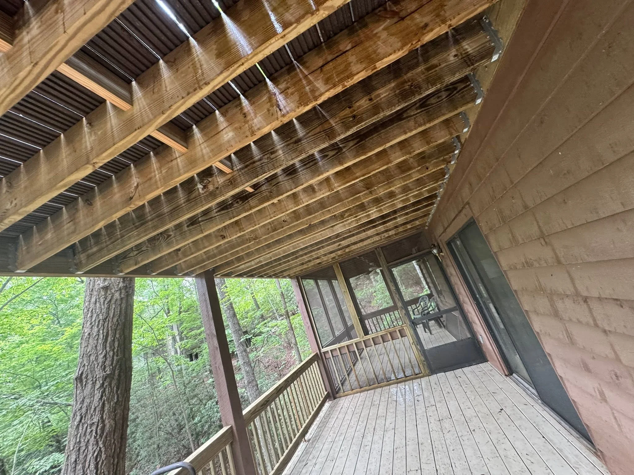 Covered deck with polycarbonate roof panels, wooden beams, and metal railings overlooking forest
