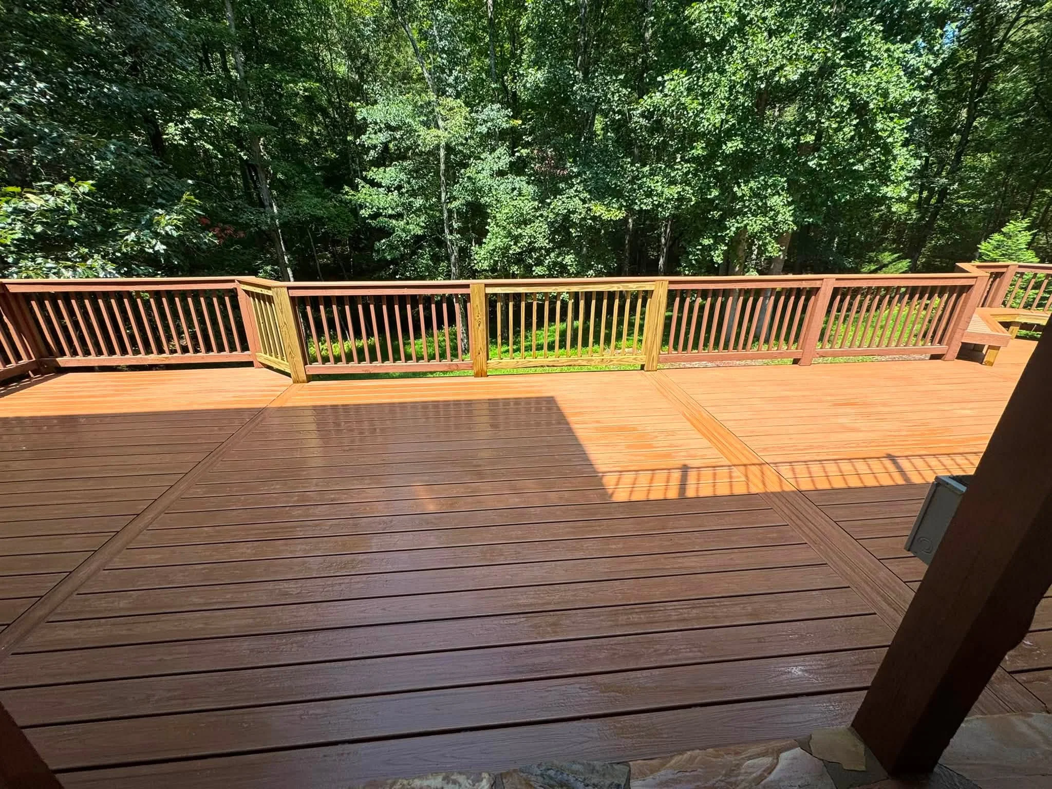 Multi-level composite deck with diagonal board pattern and vertical spindle railings overlooking forest