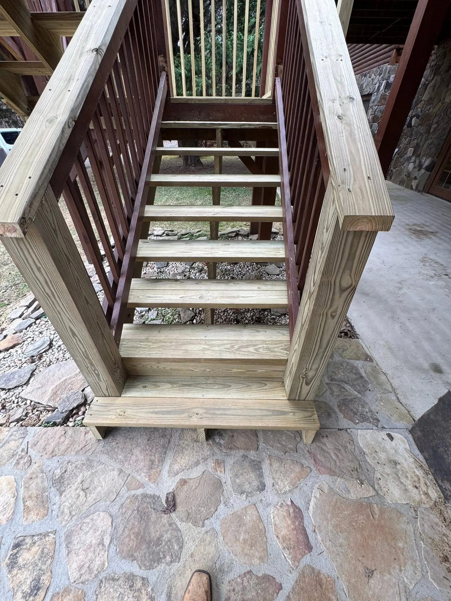 Pressure-treated wood deck stairs with railings and vertical balusters leading to stone patio