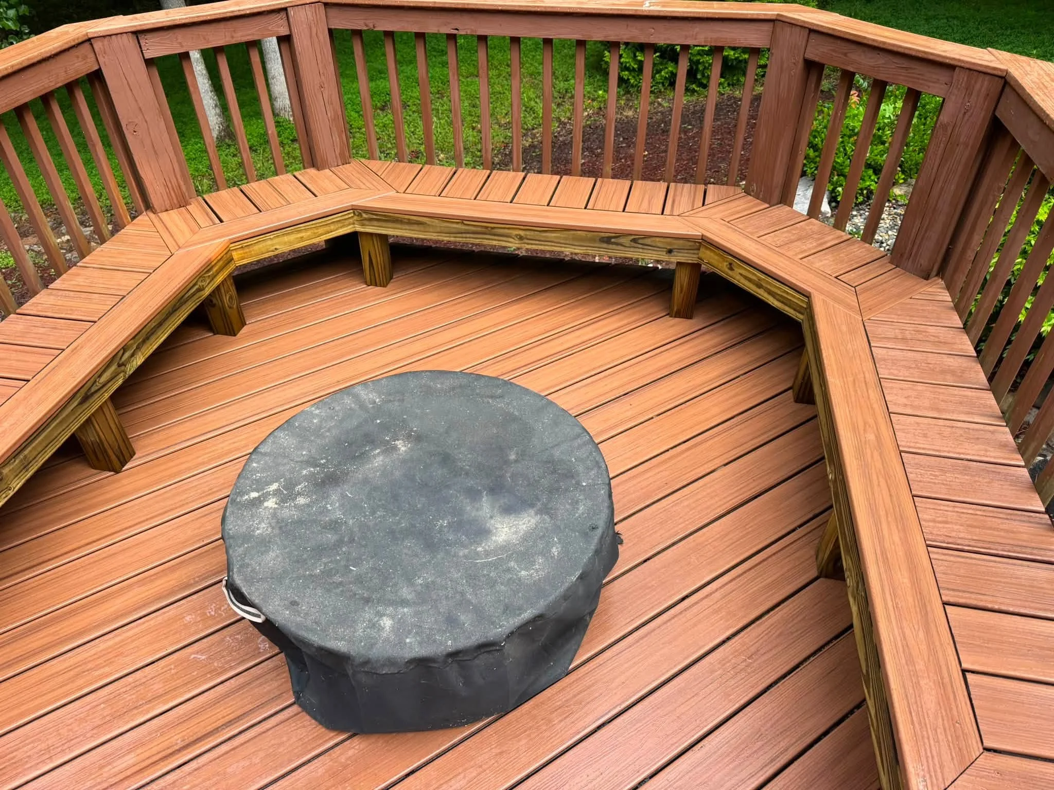 Curved composite deck with built-in bench seating and fire pit opening, cedar-tone boards with matching railings