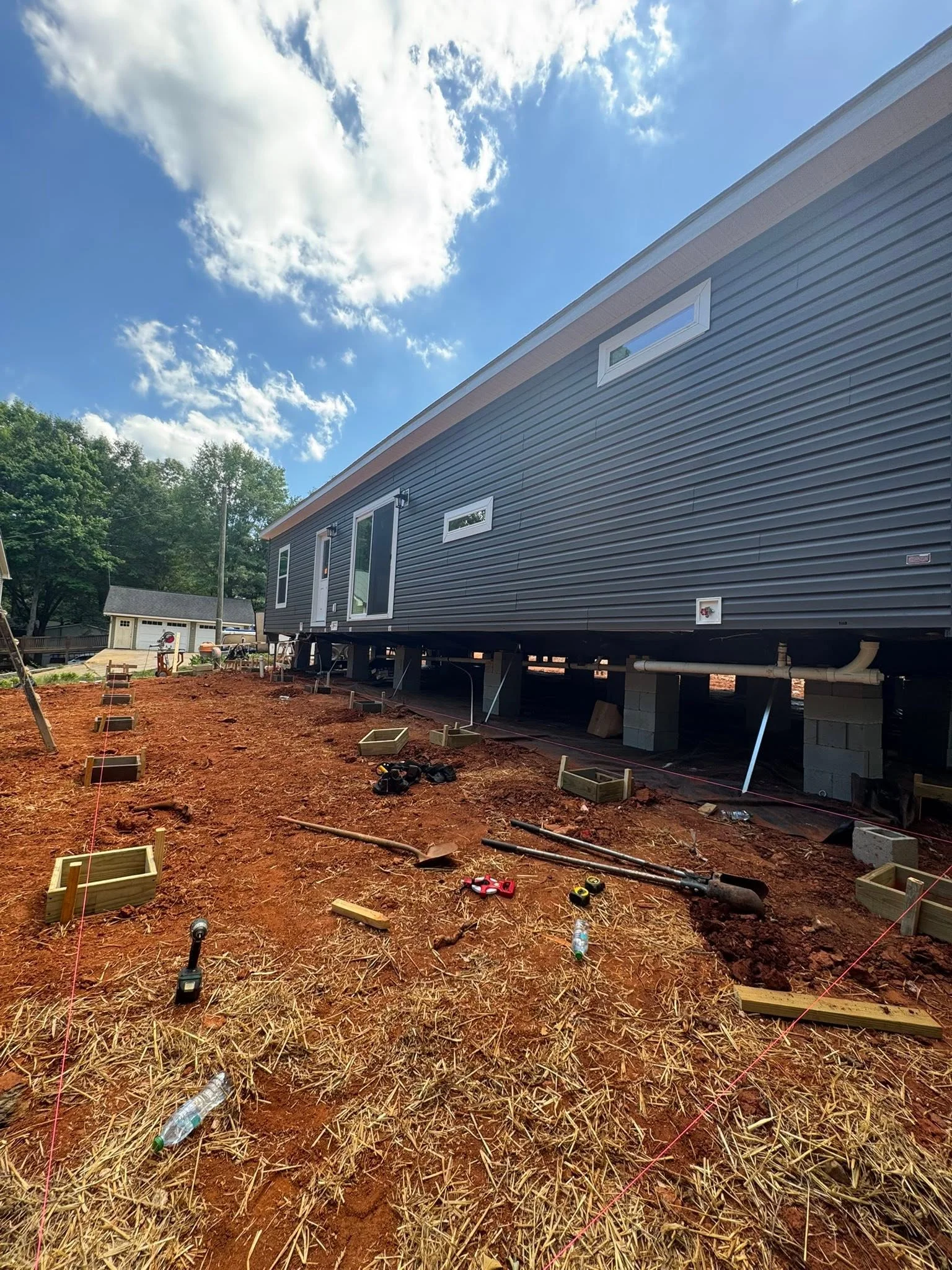 Mobile home elevated on concrete piers with pressure-treated deck framing and mulch grading