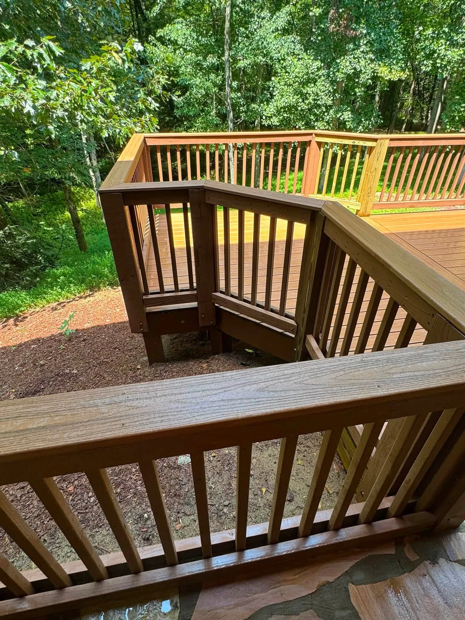 Multi-level pressure-treated deck with vertical spindle railings and integrated staircase in wooded setting