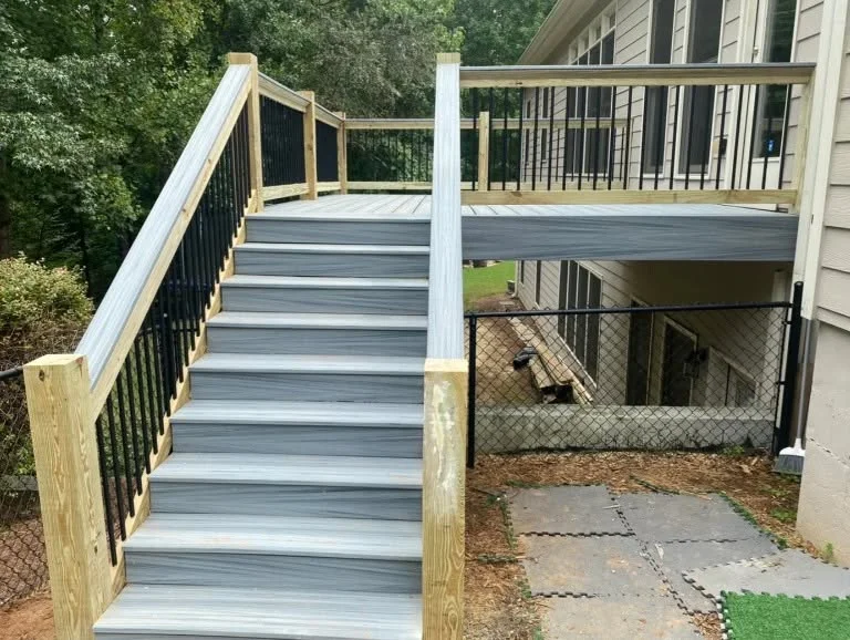 Gray composite deck with white posts, black railings, and lower level with chain-link gate