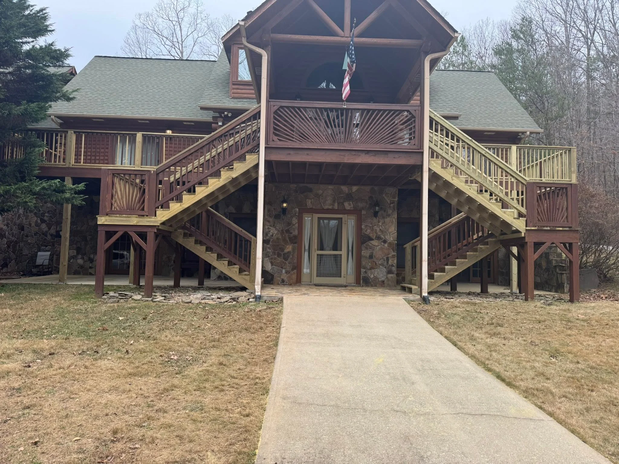Multi-level pressure-treated deck with shell-pattern railings, covered pavilion, stone base, and dual staircases