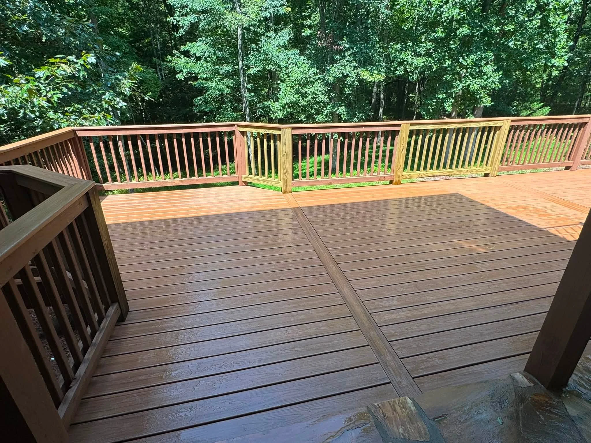 Multi-level composite deck with dark and light boards, vertical spindle railings, and forest backdrop
