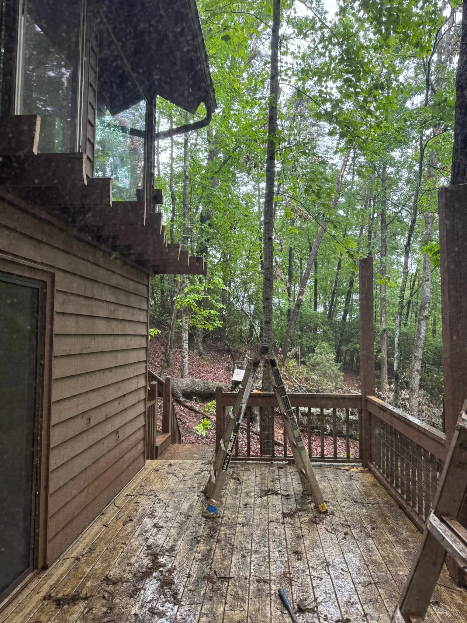Wooden deck with metal railings under construction in wooded area with ladder and tools