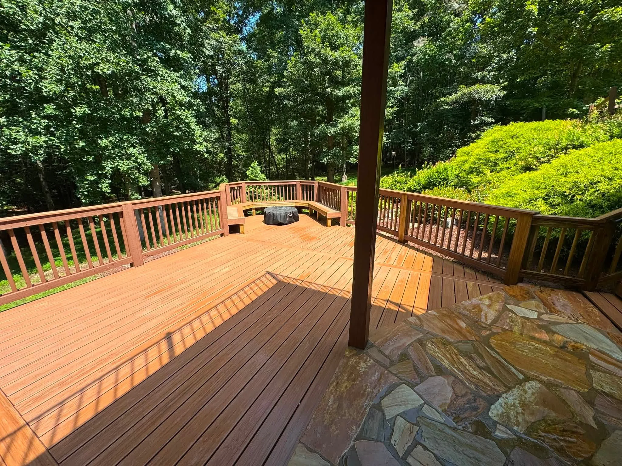 Two-tone composite deck with wood railings, stone patio, and fire pit seating area in wooded setting