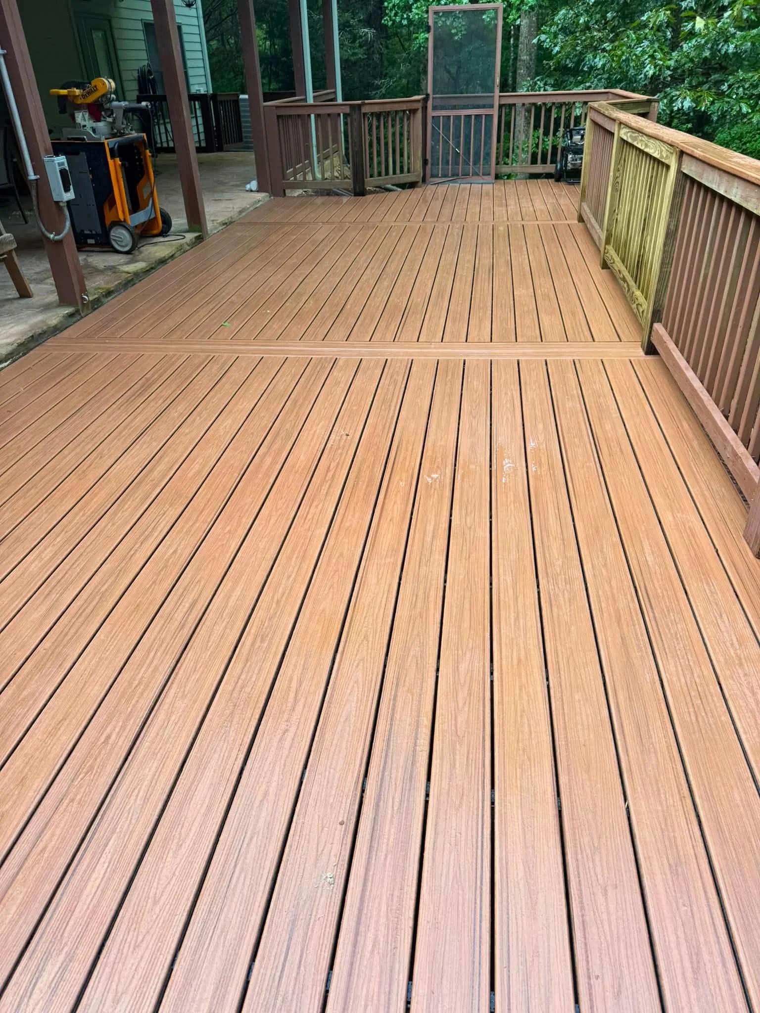 Two-level composite deck with brown boards, vertical railings, and screened porch area
