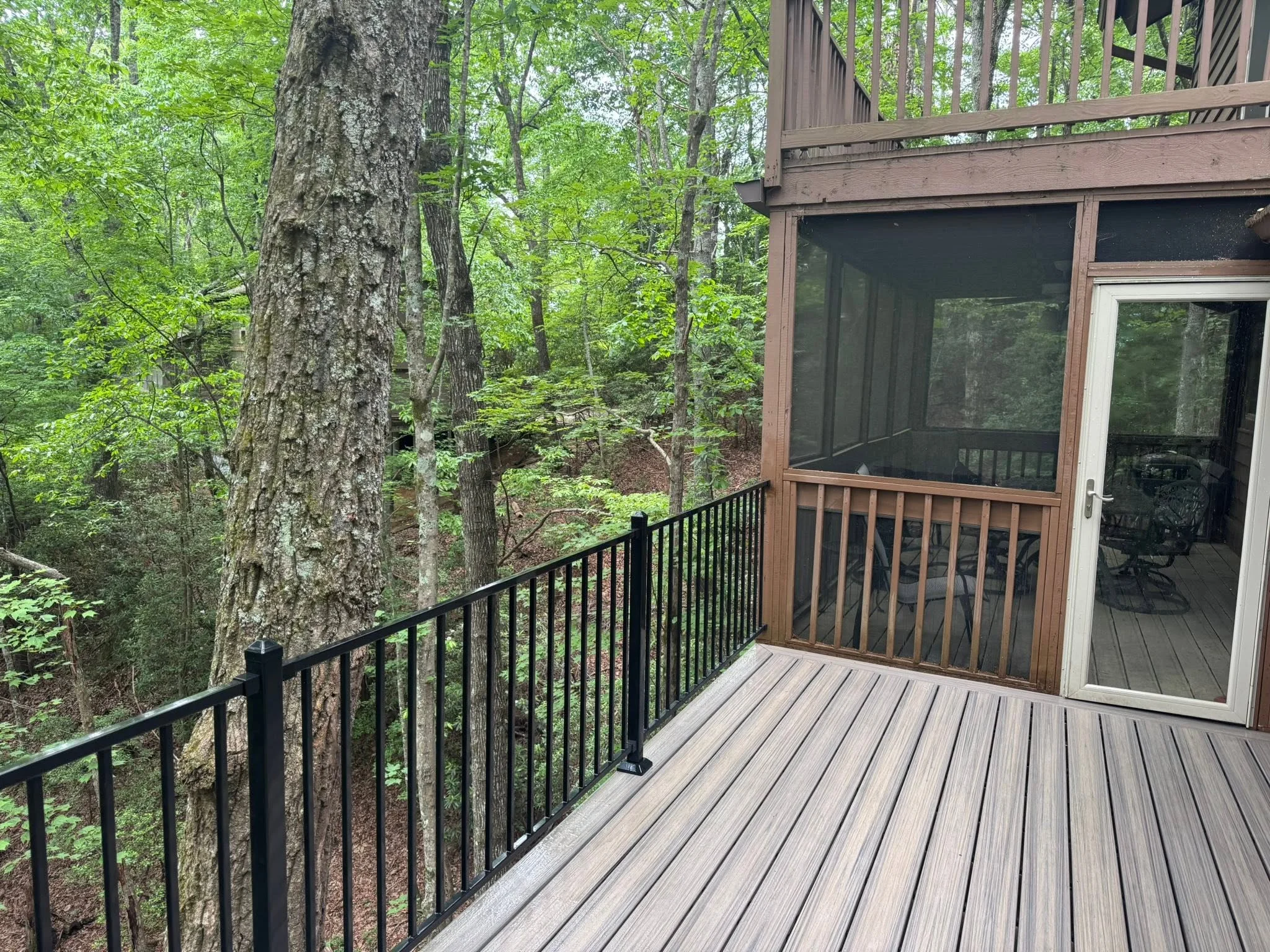 Gray composite deck with black metal railing overlooking wooded landscape, adjacent to screened porch