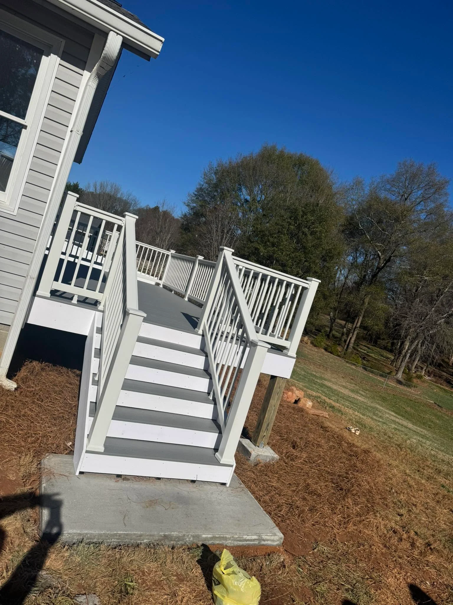 White vinyl deck with gray composite stairs, white railings, and elevated platform overlooking wooded yard