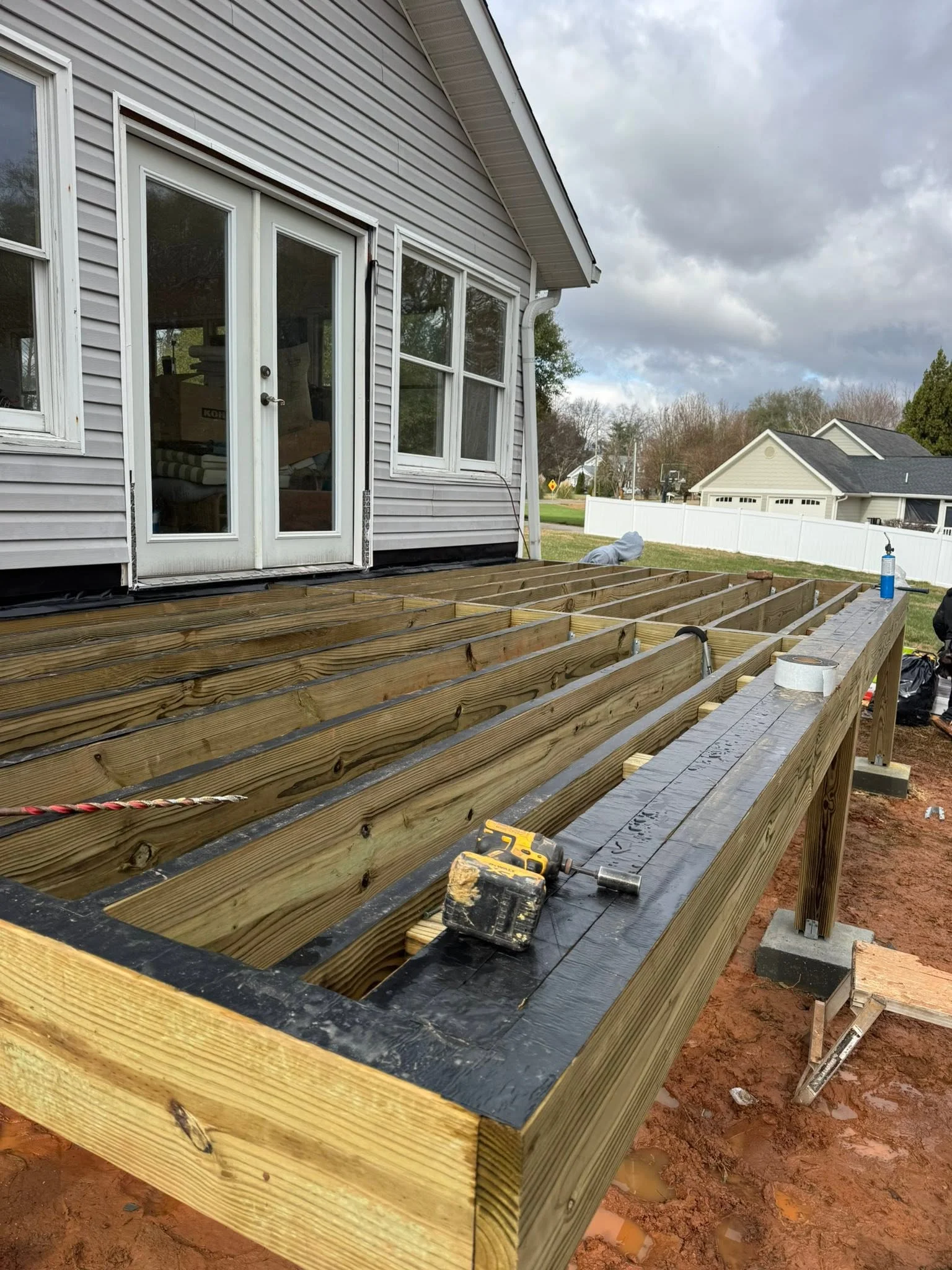 Pressure-treated wood deck frame with joists, concrete footings, and black moisture barrier during construction