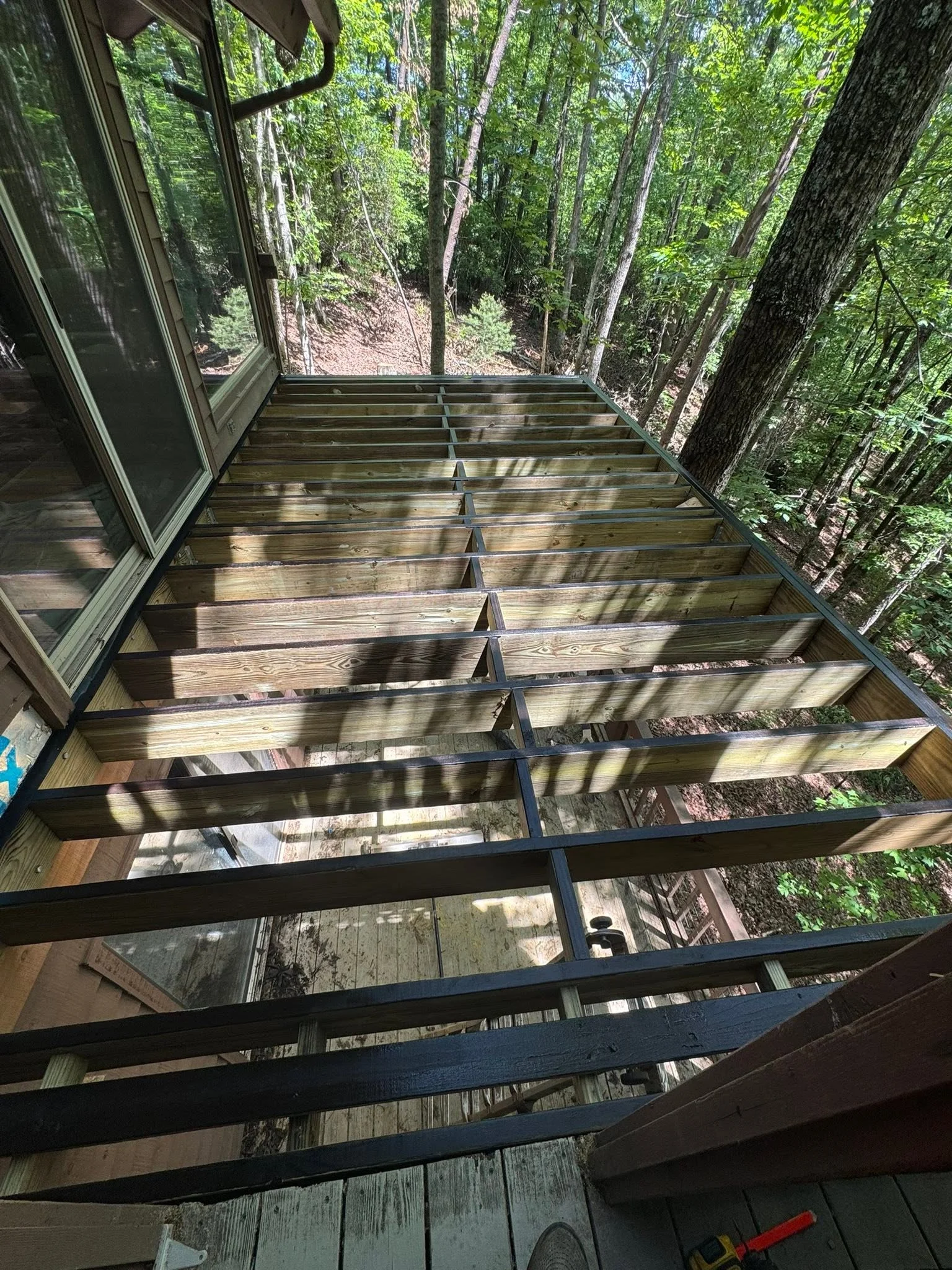 Pressure-treated deck framing with joists and steel beams in wooded setting